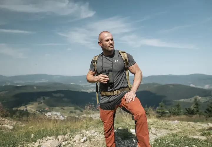 Mężczyzna w letniej czapce w góry, z lornetką w ręku, podziwia krajobraz.
