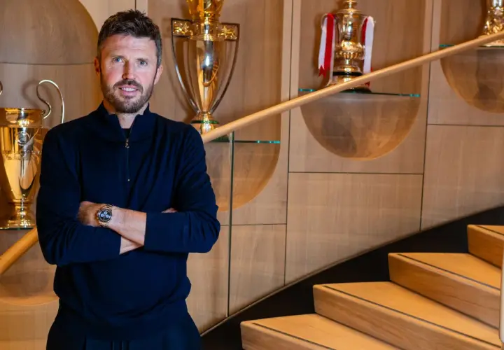 Erik ten Hag, trener Manchester United, stoi na tle pucharów, symbolizujących sukcesy klubu.