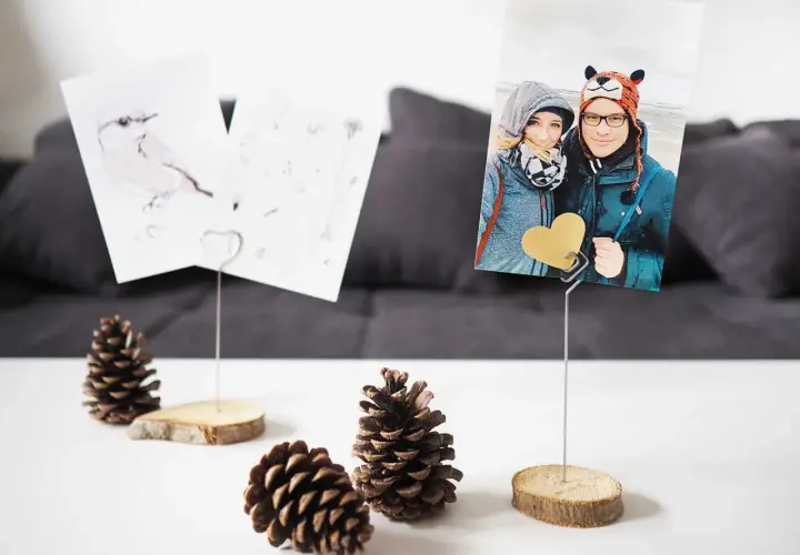 Selbstgemachte Fotohalter aus Holzscheiben und Draht mit Fotos von einem Paar und einem Vogel. Perfekt, um Erinnerungen zu präsentieren.