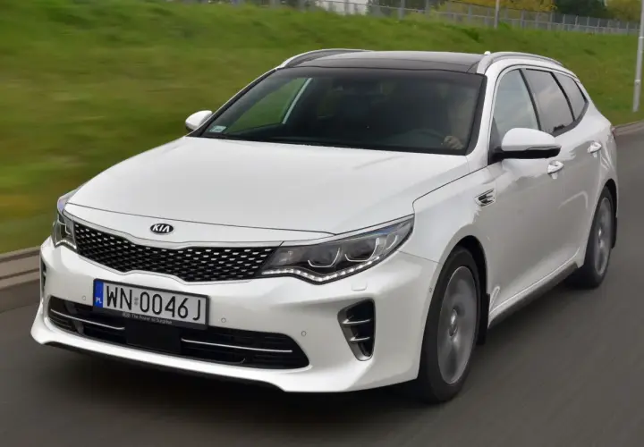 Biała Kia Optima w wersji kombi na drodze. Wiele osób szuka kia optima opinie przed zakupem.