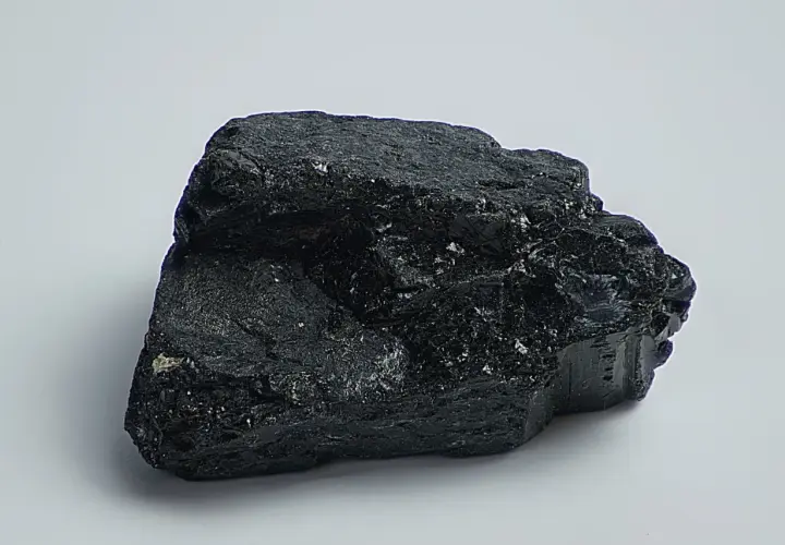 Ein glänzender, schwarzer Stein, der an einen Brocken Onyx erinnert, liegt auf weißem Grund.
