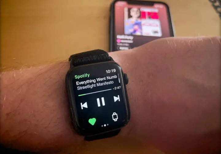 Apple Watch zeigt Spotify-Song "Everything Went Numb" von Streetlight Manifesto. Ein iPhone im Hintergrund spielt ebenfalls Musik.