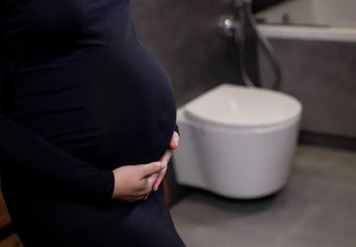Gravid kvinna med händer på magen, toalett i bakgrunden. Vanliga besvär som uvi kan drabba gravida.