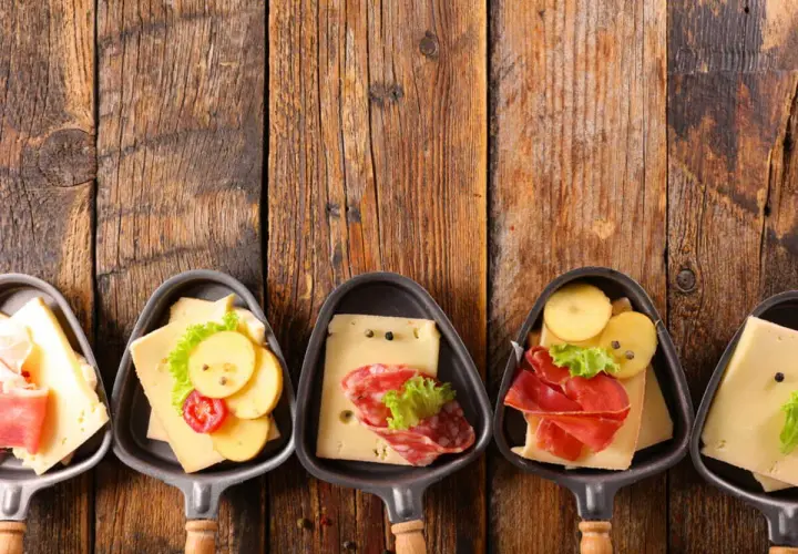 Petites coupelles pour un apéritif raclette, garnies de fromage, charcuterie et pommes de terre sur fond de bois.