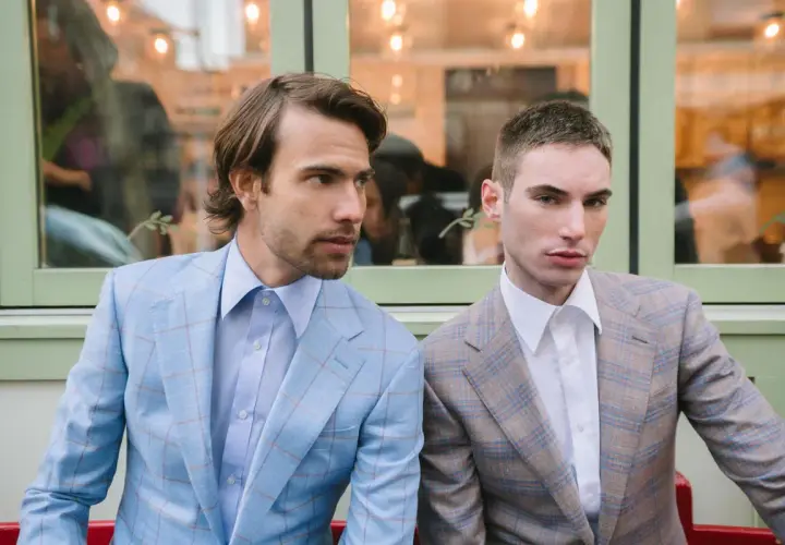Dwóch mężczyzn w garniturach w kratę. Jeden w błękitnym, drugi w brązowym. Eleganckie klapy w marynarce podkreślają ich styl.