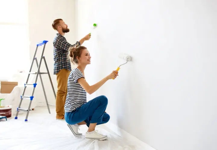 Coppia felice imbianca casa con rullo, trasformando le pareti bianche in un nuovo inizio.