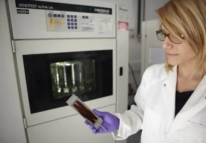 Científica con guantes morados examina una muestra de cabello en un laboratorio. Se investiga de que esta hecho el pelo para mejorar productos.