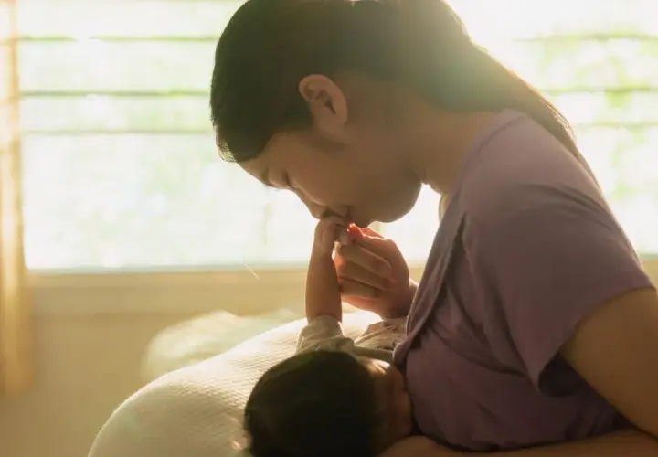 Dolce momento tra madre e neonato. La mamma bacia la manina del suo piccolo, che sembra aver mangiato troppo, sazio e felice.