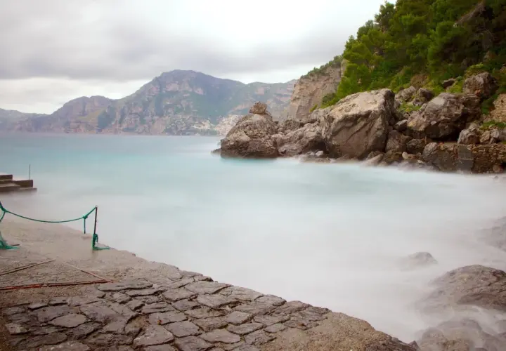 Vue brumeuse de la côte rocheuse de Praiano, Italie, avec des vagues douces et des montagnes en arrière-plan.