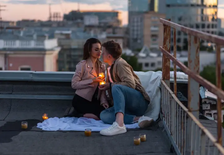 Romantyczny wieczór na dachu. Para trzyma świece, patrząc sobie w oczy. Czy napisać pierwsza do faceta?