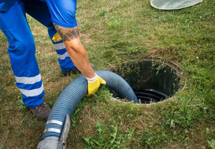 Pracownik w żółtych rękawiczkach wkłada gruby wąż do szamba, pokazując, jak zrobić odpływ.