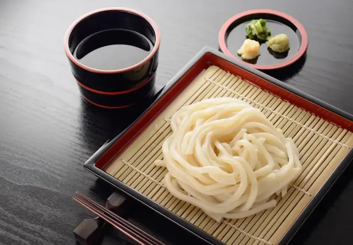 Prosty makaron udon przepis: grube kluski na bambusowej macie, miseczka z sosem i dodatkami. Idealne danie.