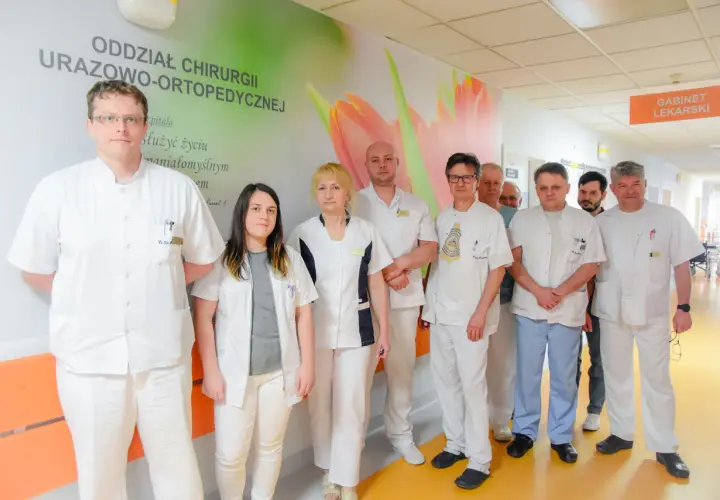 Grupa lekarzy w białych fartuchach stoi w szpitalnym korytarzu.