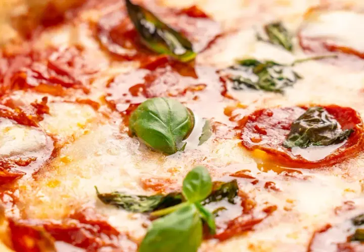 Nahaufnahme einer Pizza mit geschmolzenem Käse, roten Salami-Scheiben und frischem Basilikum. Verschiedene Salami-Sorten machen diese Pizza unwiderstehlich.