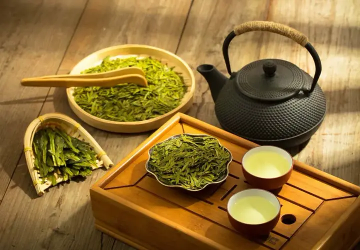 Zaparzanie sencha green tea. Suszone liście, czajniczek i dwie filiżanki z naparem na drewnianej tacce.