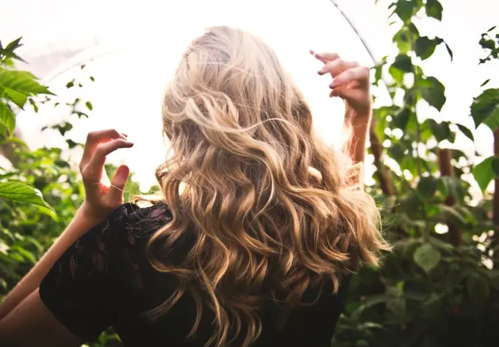 Blondes Haar mit Beach Waves im Sonnenlicht, umgeben von grünen Blättern.