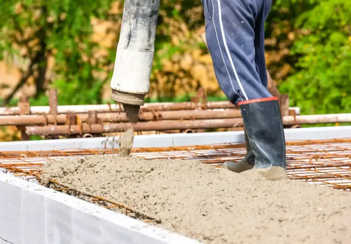 Beton c25/30 wylewany z pompy na zbrojenie. Pracownik w gumowcach stoi w świeżym betonie.