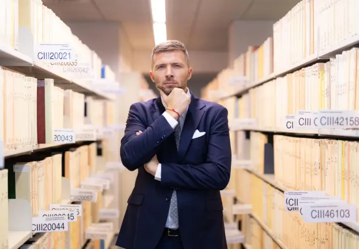 Mężczyzna w garniturze zastanawia się, jak liczyć 6 miesięcy na odrzucenie spadku, wśród regałów pełnych akt.