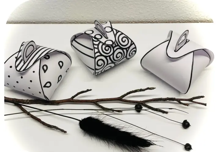 Drei selbstgebastelte Geschenkboxen mit Mustern, inspiriert von Vorlagen zum Geschenkbox selber basteln. Ein Ast und schwarze Federn liegen daneben.