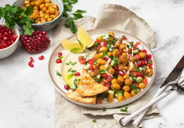 Bunter Kichererbsen Salat mit Granatapfelkernen, Tomaten, Gurken und Hummus, garniert mit Minze und serviert mit Pitabrot.