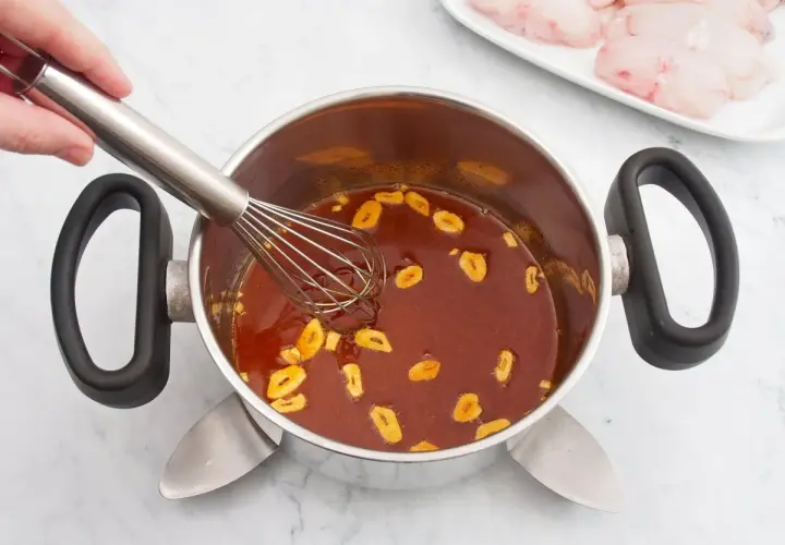 Batir salsa con ajo en una olla. En un plato, trozos de rape fisch listos para cocinar.