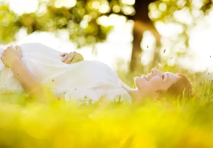 Une femme enceinte, baignée par le soleil, sourit en se prélassant dans l'herbe verte.