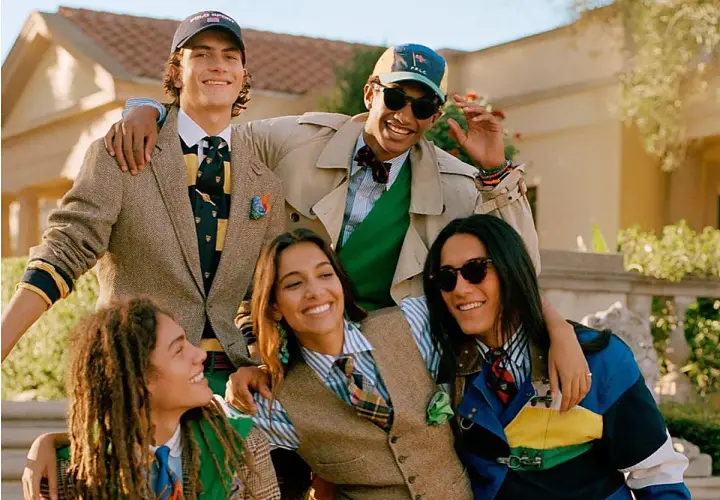 Grupo de jóvenes sonriendo, vestidos con estilo preppy: trajes, corbatas, chalecos y gorras.