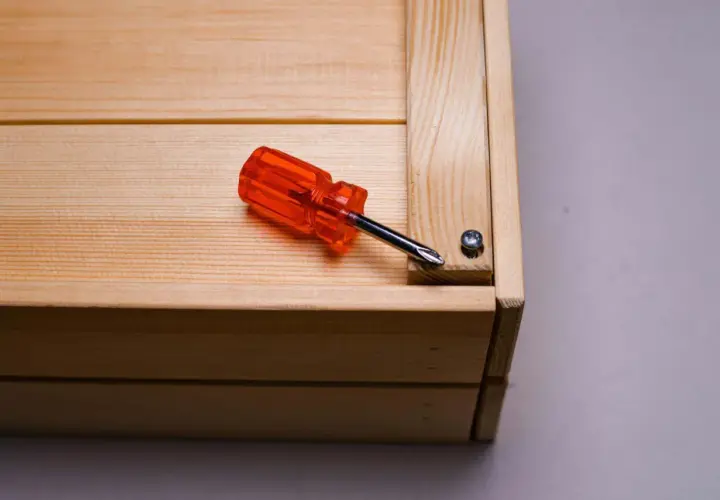 Cacciavite arancione su un mobile in legno grezzo, pronto per essere restaurato.