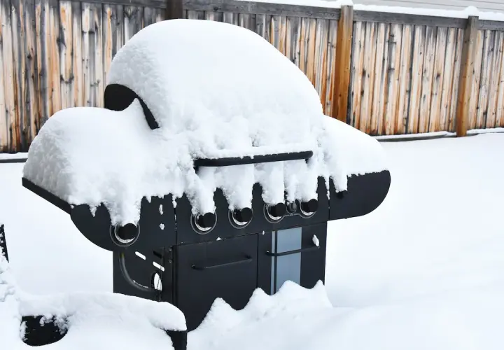 En snötäckt gasolgrill under tak, redo för sommarens grillkvällar trots vinterns kyla.