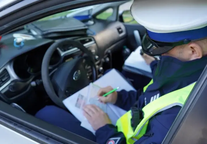 Policjant w radiowozie spisuje mandat za jazdę bez kasku.