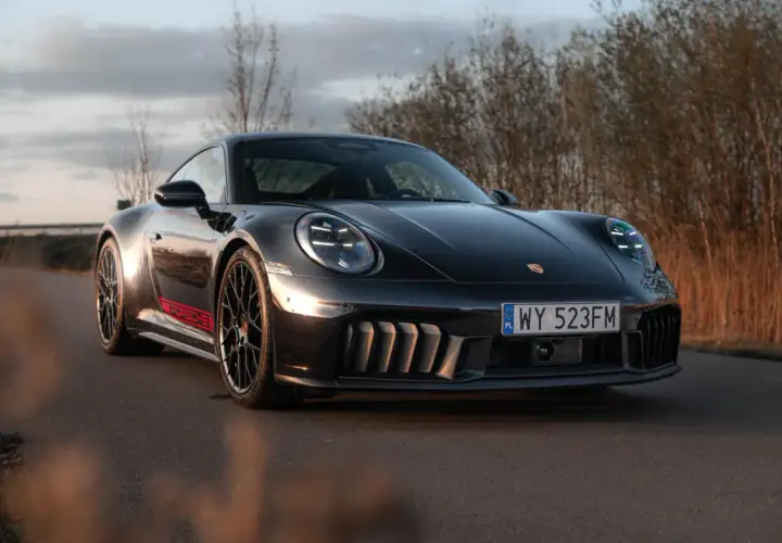 Czarny Porsche GTS z czerwonymi akcentami na progu, zaparkowany na drodze wśród suchych traw.