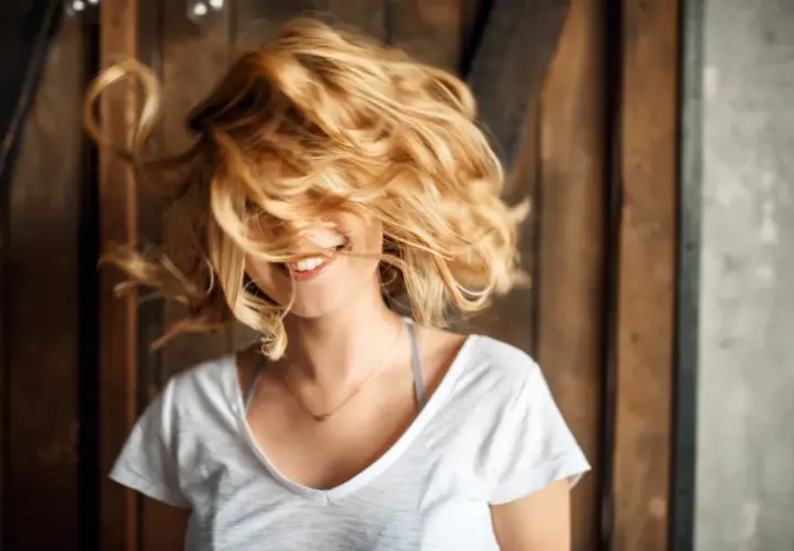 Uśmiechnięta dziewczyna z burzą włosów w odcieniu maślany blond, które wirują wokół jej twarzy.