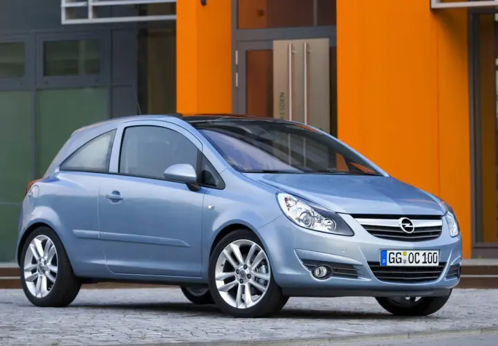 Niebieski Opel Corsa D 1.2 benzyna stoi przed pomarańczowym budynkiem.