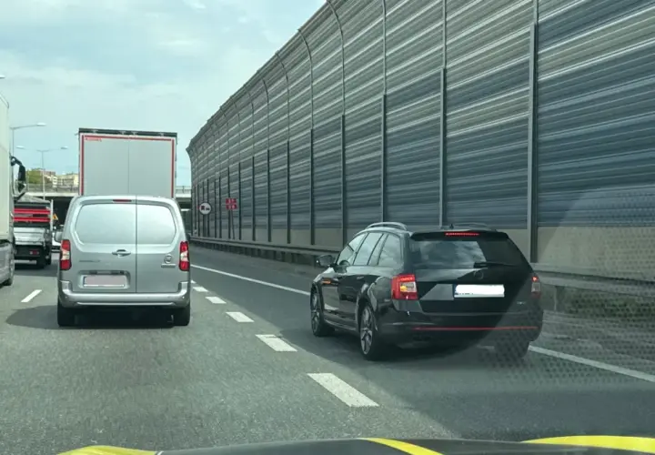 Kork na autostradzie, samochody i ciężarówki stoją w korku. Widać znak informujący o jeździe na suwak.