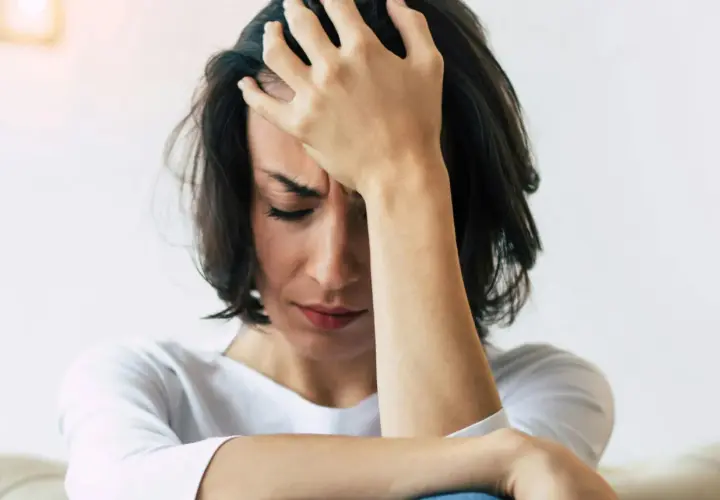 En kvinna med handen mot pannan, ansiktet nedåt, visar tydliga tecken på depression och dess fysiska symptom som huvudvärk och utmattning.