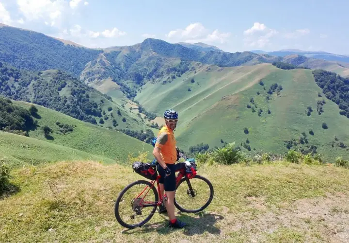 Ciclista con su bicicleta de gravel en un paisaje montañoso verde, disfrutando de la ruta transpirenaica.