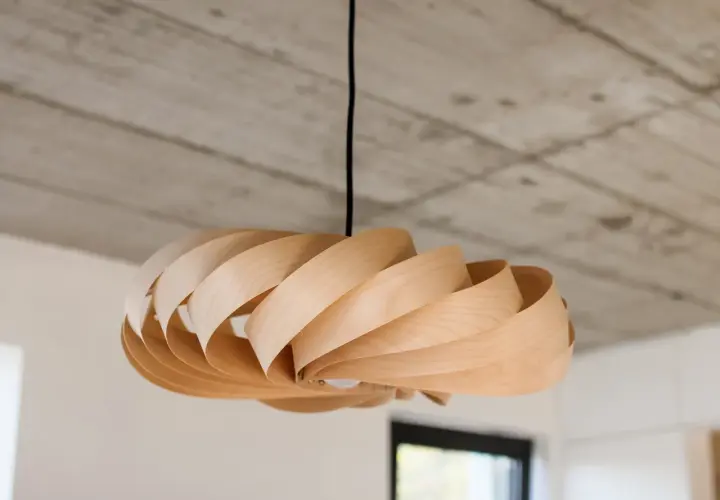 Drewniana lampka DIY o spiralnym kształcie, zawieszona pod betonowym sufitem.