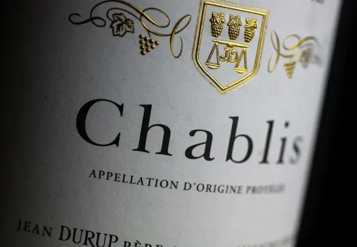 Gros plan sur une étiquette de vin Chablis, avec un blason doré orné de grappes de raisin et d'une balance. L'appellation d'origine protégée est clairement visible.