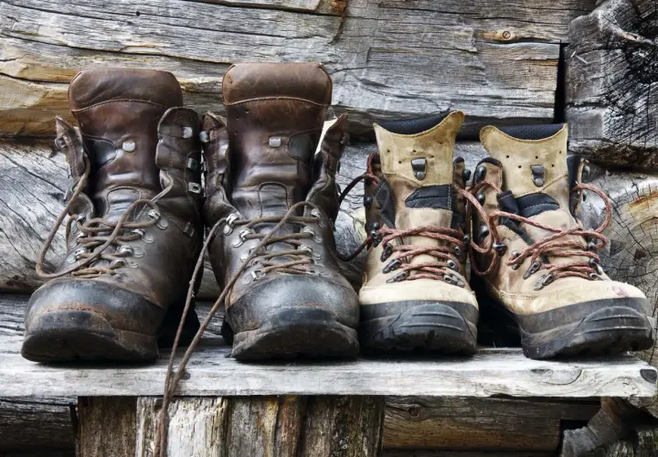 Four pairs of hiking boots, two dark brown leather and two tan, sit on a wooden shelf. Considering if you should size up in hiking shoes?