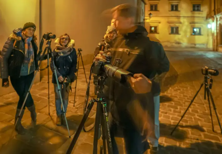 Uczestnicy kursu fotografii dla początkujących ćwiczą nocne zdjęcia na brukowanej uliczce.