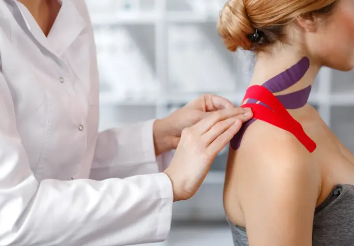Fizjoterapeuta zakłada taśmy na szyję pacjentki. Warto znać kinesiotaping przeciwwskazania, by uniknąć problemów.