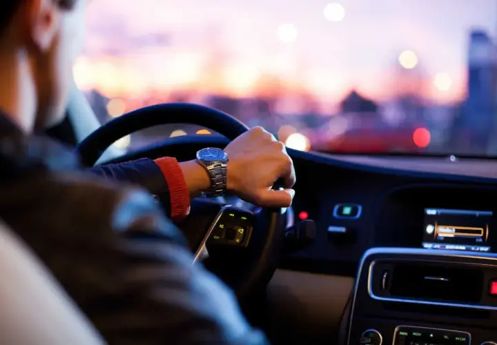 Mano al volante, orologio elegante, tramonto sfocato. Una guida esperta affronta la sera con sicurezza.