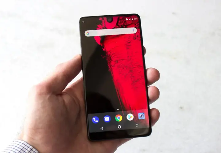 Dłoń trzyma smartfon z wycięciem (notch) na górze ekranu, wyświetlający czerwony wzór i ikonki Androida.