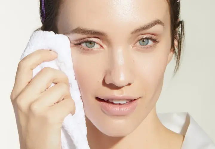 Mujer con toalla blanca limpiando su rostro, evitando el maquillaje cuarteado.