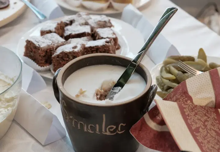 Gęsty smalec w glinianym naczyniu, obok ciasto czekoladowe i ogórki.