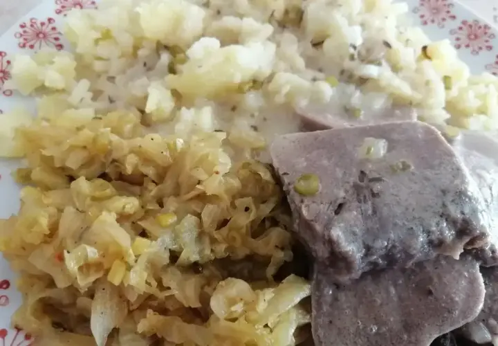 Na talerzu ułożone są plastry gotowanych ozorków w sosie, obok porcja ziemniaków i duszona kapusta.