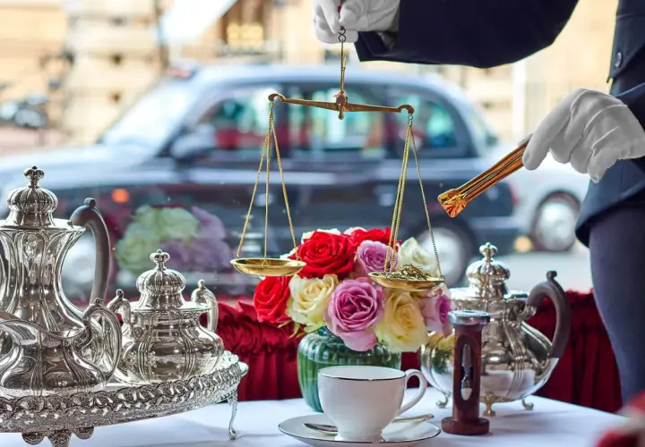 En elegant uppsättning för klassisk afternoon tea med silverkannor, en blomsterbukett och en våg för att mäta teblad.