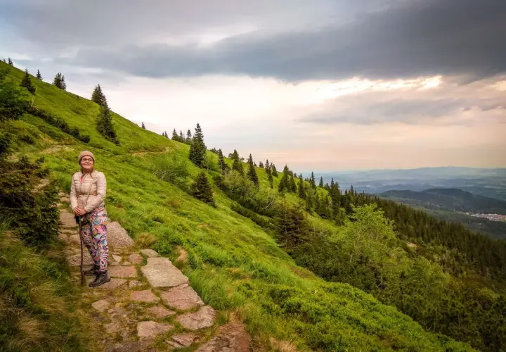 Kobieta na kamiennym szlaku, podziwiająca widok z zielonego zbocza. W oddali widać lasy i góry, a nad nimi burzowe chmury. To piękny widok ze **śnieżka szczyt**.