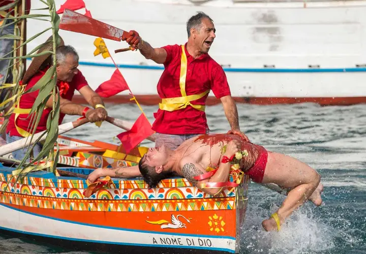 Uomo in barca siciliana, coperto di rosso, durante le feste. Un rematore con remo insanguinato.