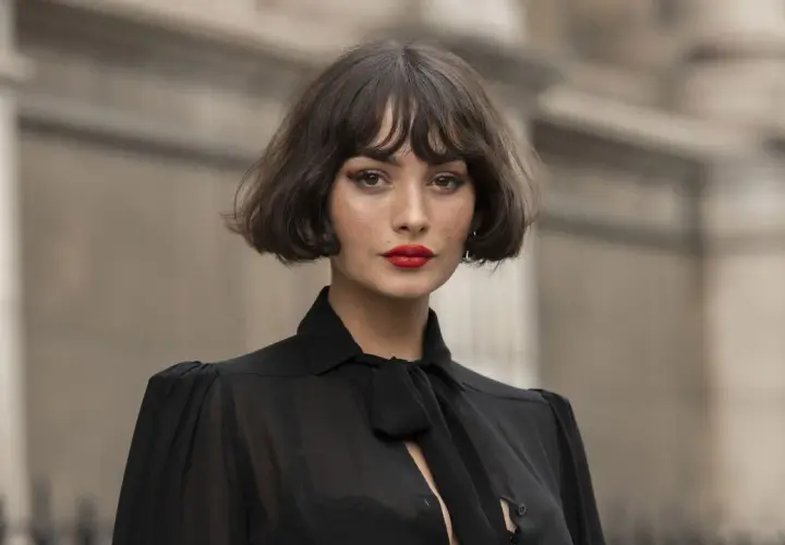 Mujer con un elegante corte de pelo **french bob**, labios rojos vibrantes y un top negro con lazada.